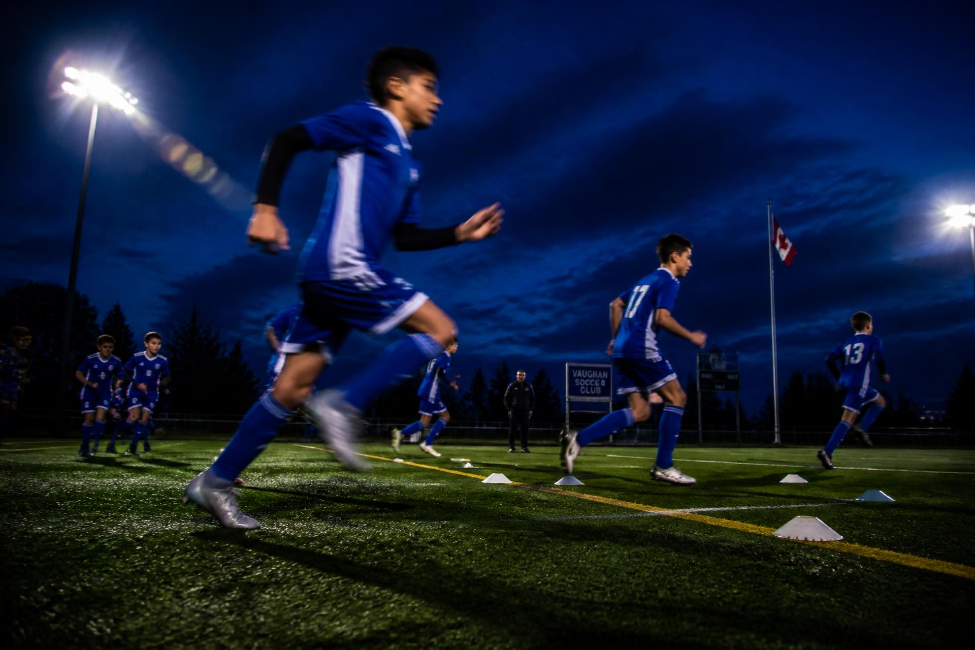 ProStars FC youth players sprinting through a floodlit training session at dusk